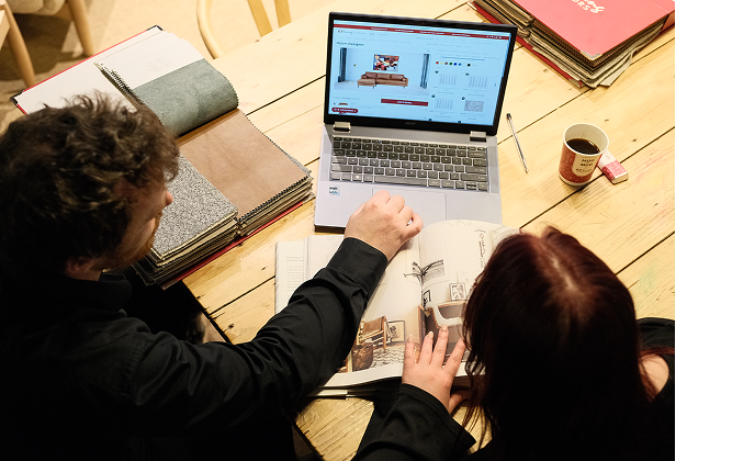 Two people choosing fabric swatches while browsing furniture on a laptop